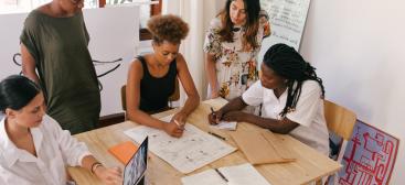 cinq personnes réunis autour d'une table, en train de regarder des papiers pour réaliser un projet ou une présentation