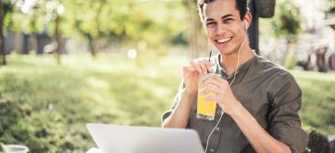 étudiant fixant la caméra avec le sourire, assis avec un verre de jus d'orange à la main
