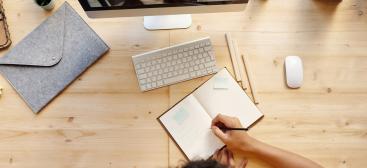 Une personne prend des notes sur un cahier tout en regardant une vidéo sur son ordinateur