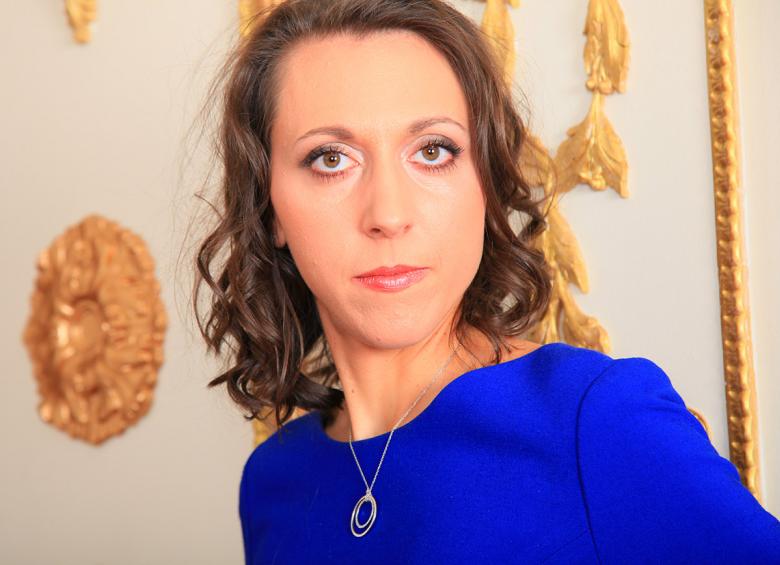 Photo d'Aude Bonord en bleu devant une boiserie blanche aux motifs dorés
